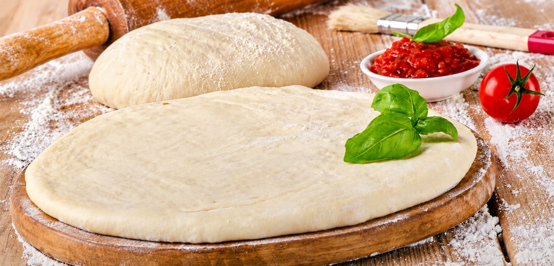 Pâte à pizza fraîche étalée sur un plan de travail fariné